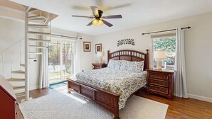 A bedroom with a wooden bed, a ceiling fan, a staircase, and a window with curtains.