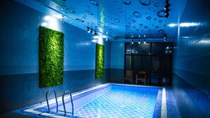 Piscina interna com piso ladrilhado, parede verde e teto com gotas d'água.