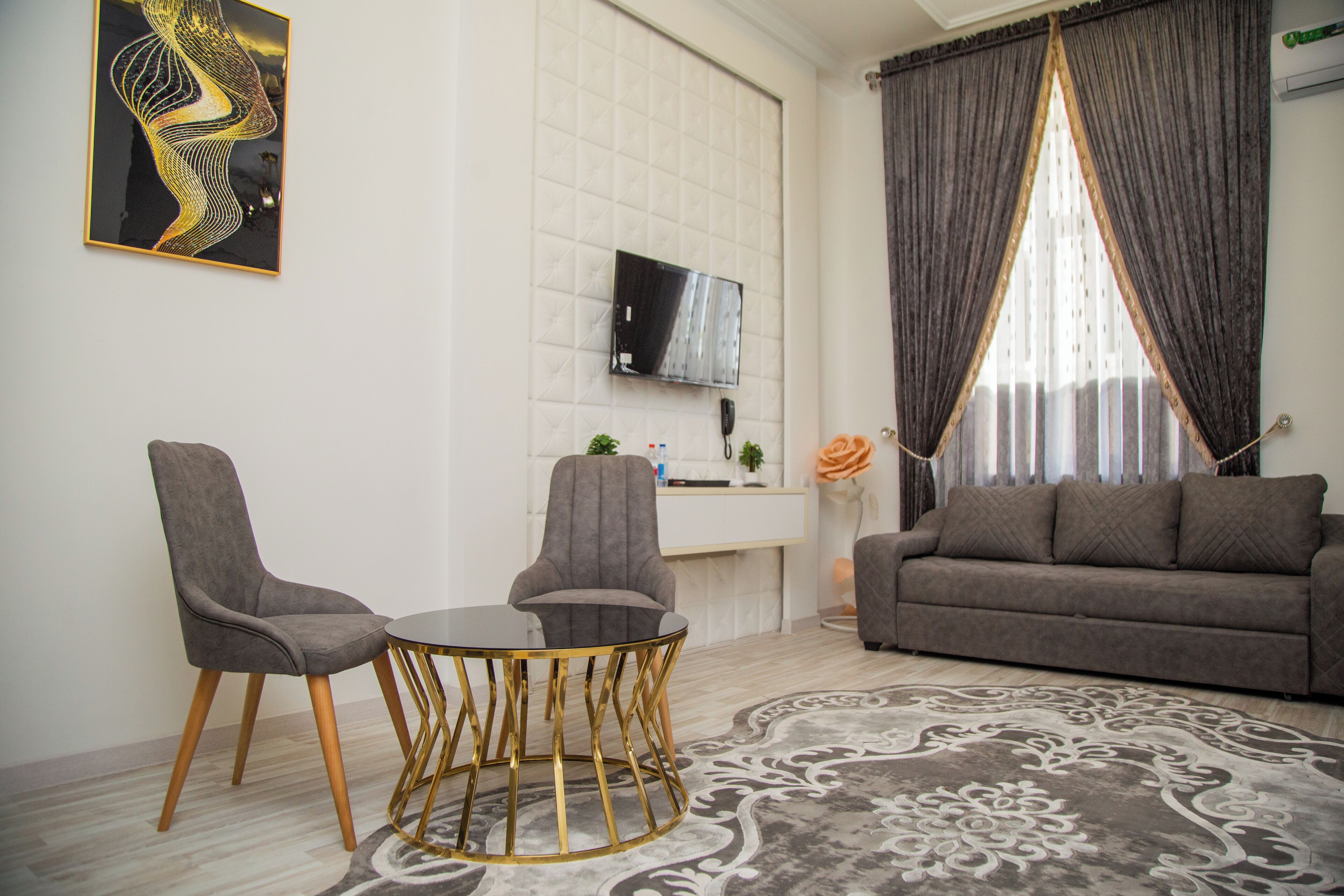 A modern living room with a sofa, two armchairs, a coffee table, and a TV mounted on the wall.