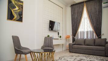 A modern living room with a sofa, two armchairs, a coffee table, and a TV mounted on the wall.
