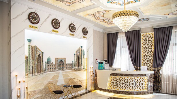 Um hall luxuoso com balcão de recepção, um candelabro e um espelho grande refletindo a paisagem urbana.