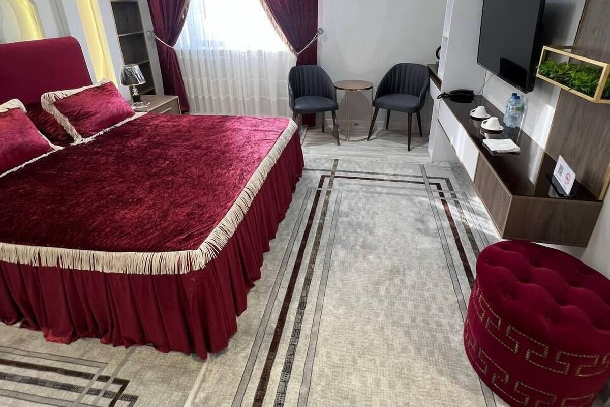 A modern bedroom with a large bed, a TV, a desk, and a chair.