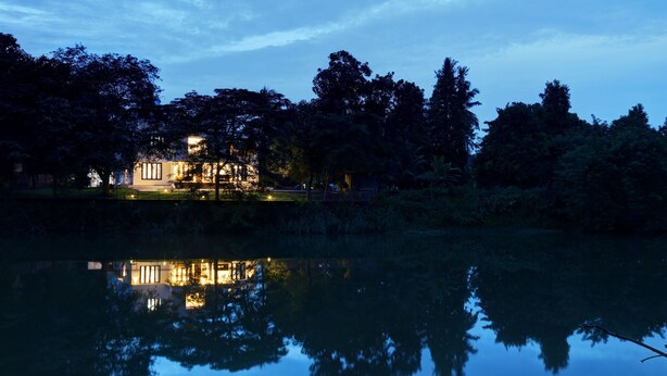 A lakeside hotel with a reflection in the water, surrounded by trees and a clear sky.