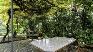 A covered outdoor seating area with a table and chairs, surrounded by dense foliage. - Villa Visconta in Naresso Inferiore (Besana in Brianza)