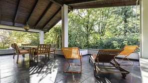 A covered patio with a wooden table and chairs, surrounded by lush greenery. - Villa Visconta in Naresso Inferiore (Besana in Brianza)