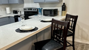 Une cuisine moderne avec des meubles gris, un plan de travail blanc et une table à manger en bois accompagnée de deux chaises.
