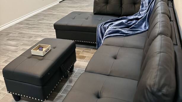 Un salon moderne avec un canapé d’angle, un pouf et une petite table d’appoint en bois.
