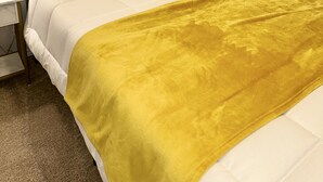 Un lit bien fait, avec du linge de lit blanc et un plaid jaune, une tête de lit verte et une lampe de chevet.