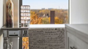 Una habitación con un escritorio, un florero con ramas y una ventana que ofrece vistas a un paisaje.