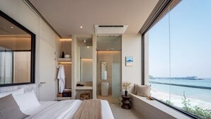 Ett modernt hotellrum med en stor säng, en rymlig klädkammare och ett badrum med en duschkabin i glas, samt utsikt över havet.