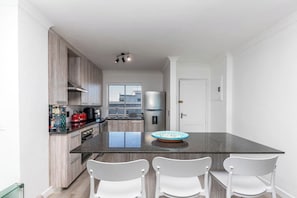 A modern kitchen with a central island, white chairs, and a large window.