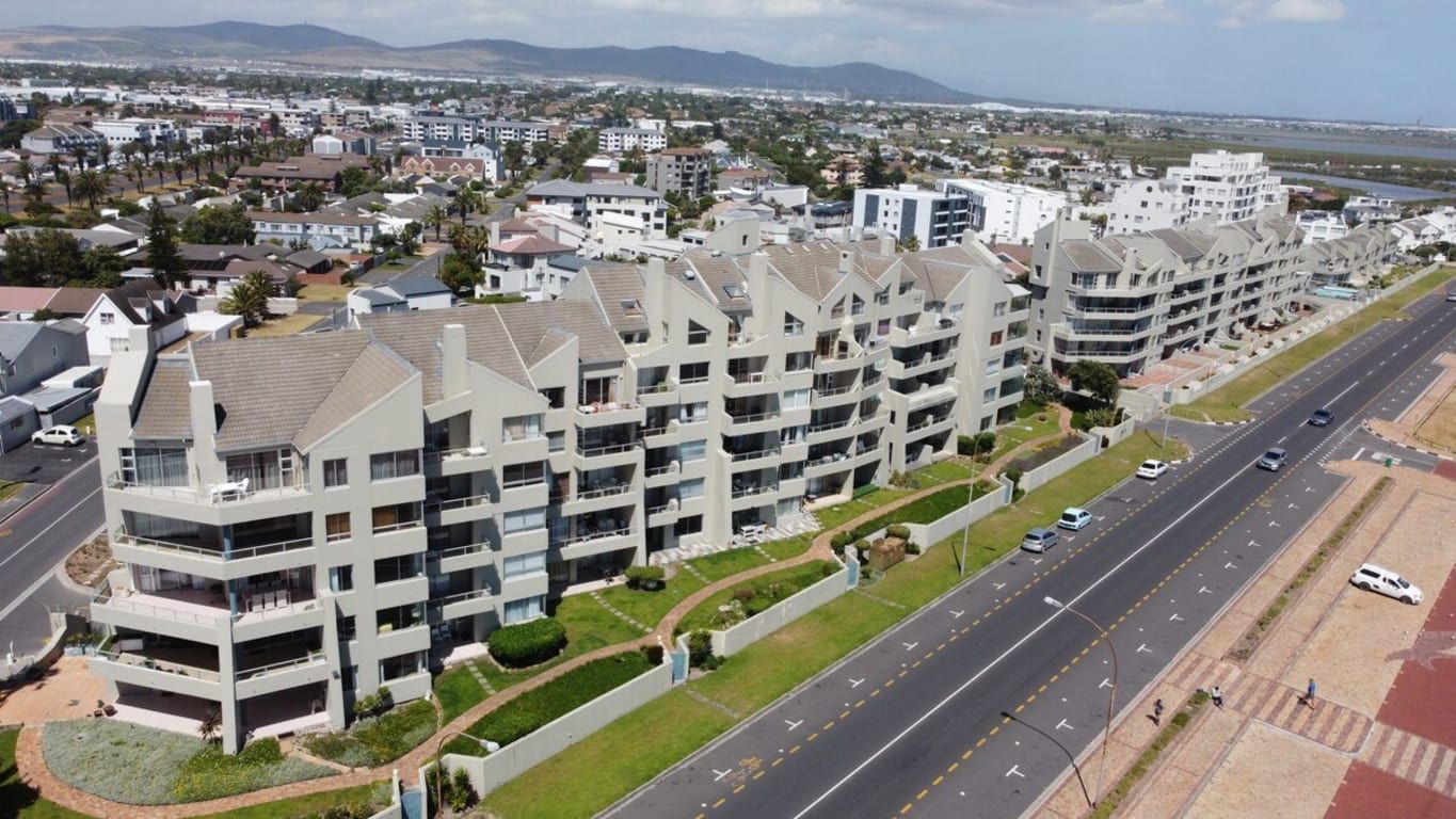 A modern apartment complex with multiple floors, a central courtyard, and a road adjacent to the buildings.