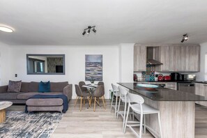 A modern living room with a sofa, dining area, and kitchen with wooden cabinets.