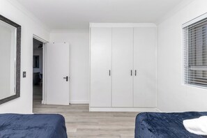 Ein Schlafzimmer mit zwei Betten, einem Kleiderschrank, einem Spiegel und einem Fenster mit Jalousien.