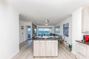 A modern kitchen with a central island, large windows, and a view of the sea.