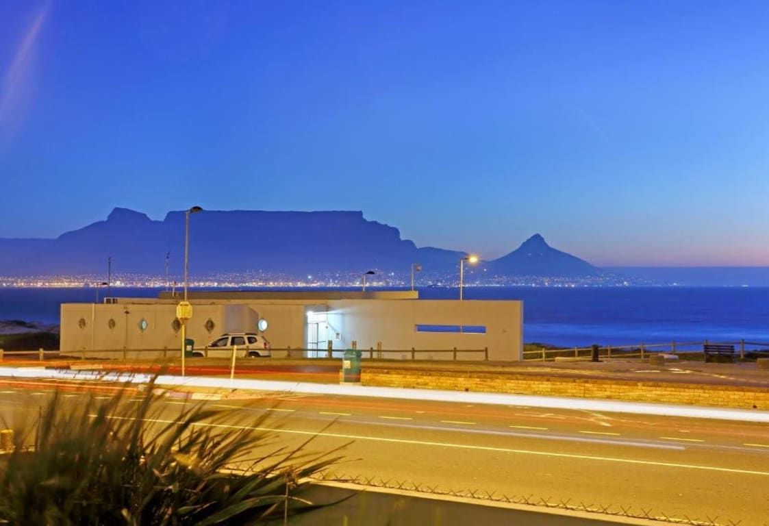 A coastal road with a building in the foreground and a mountain in the background.