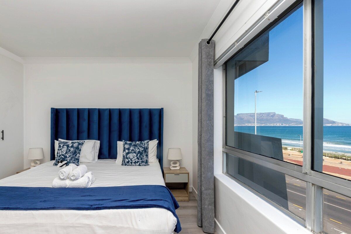 A hotel room with a large bed, two bedside tables, and a view of the ocean.