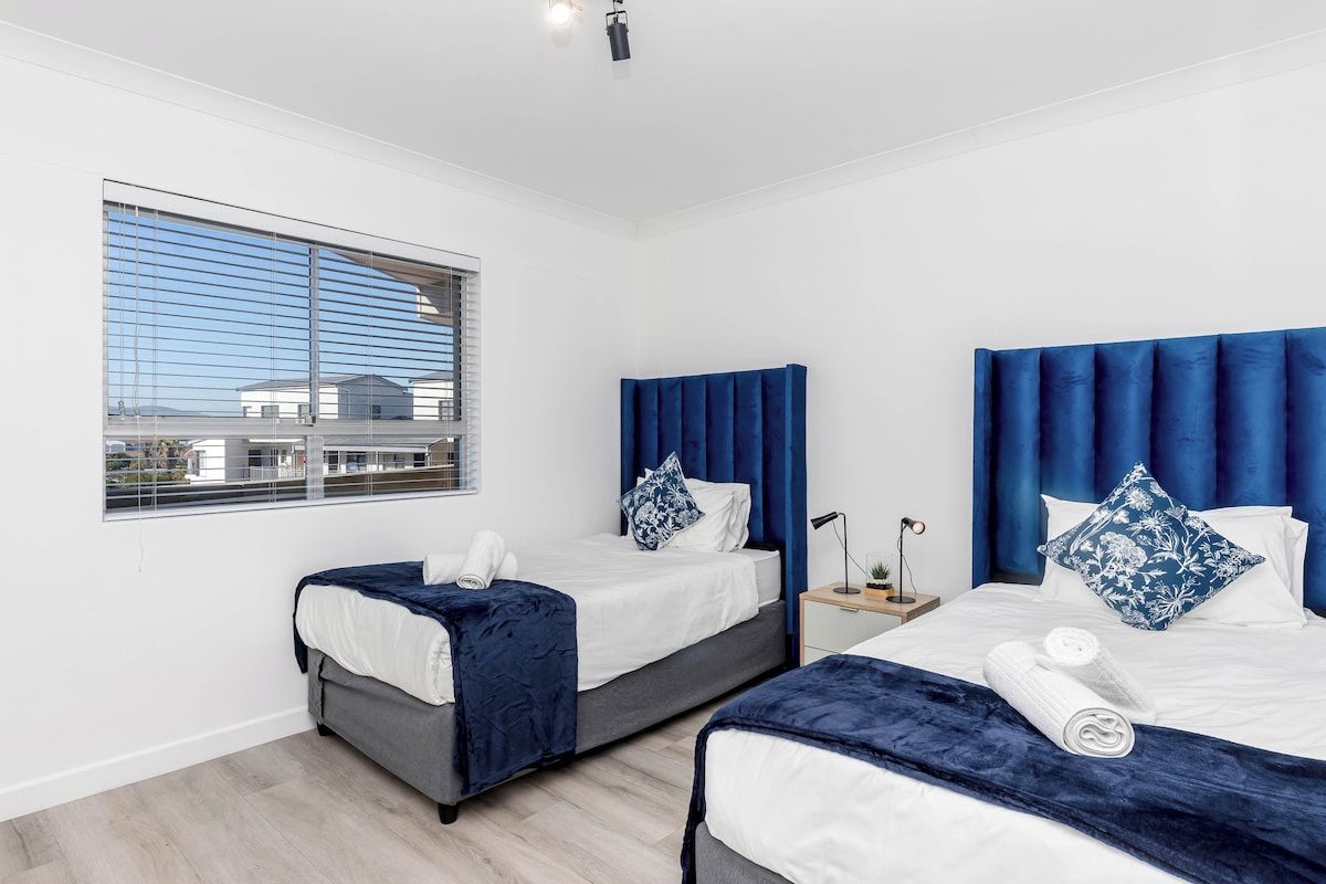 Quarto de hotel moderno com duas camas, uma janela grande e vista para prédios.