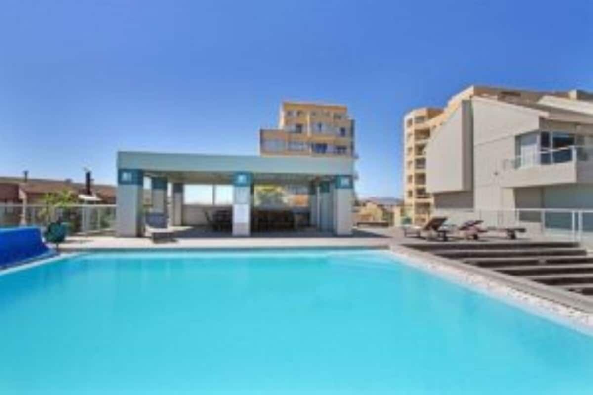 A modern hotel with a swimming pool, a covered area, and a multi-story building in the background.