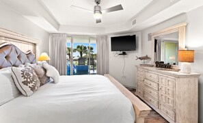 Relax in comfort with a large bed, flat-screen TV, and a balcony offering a serene view of palm trees.