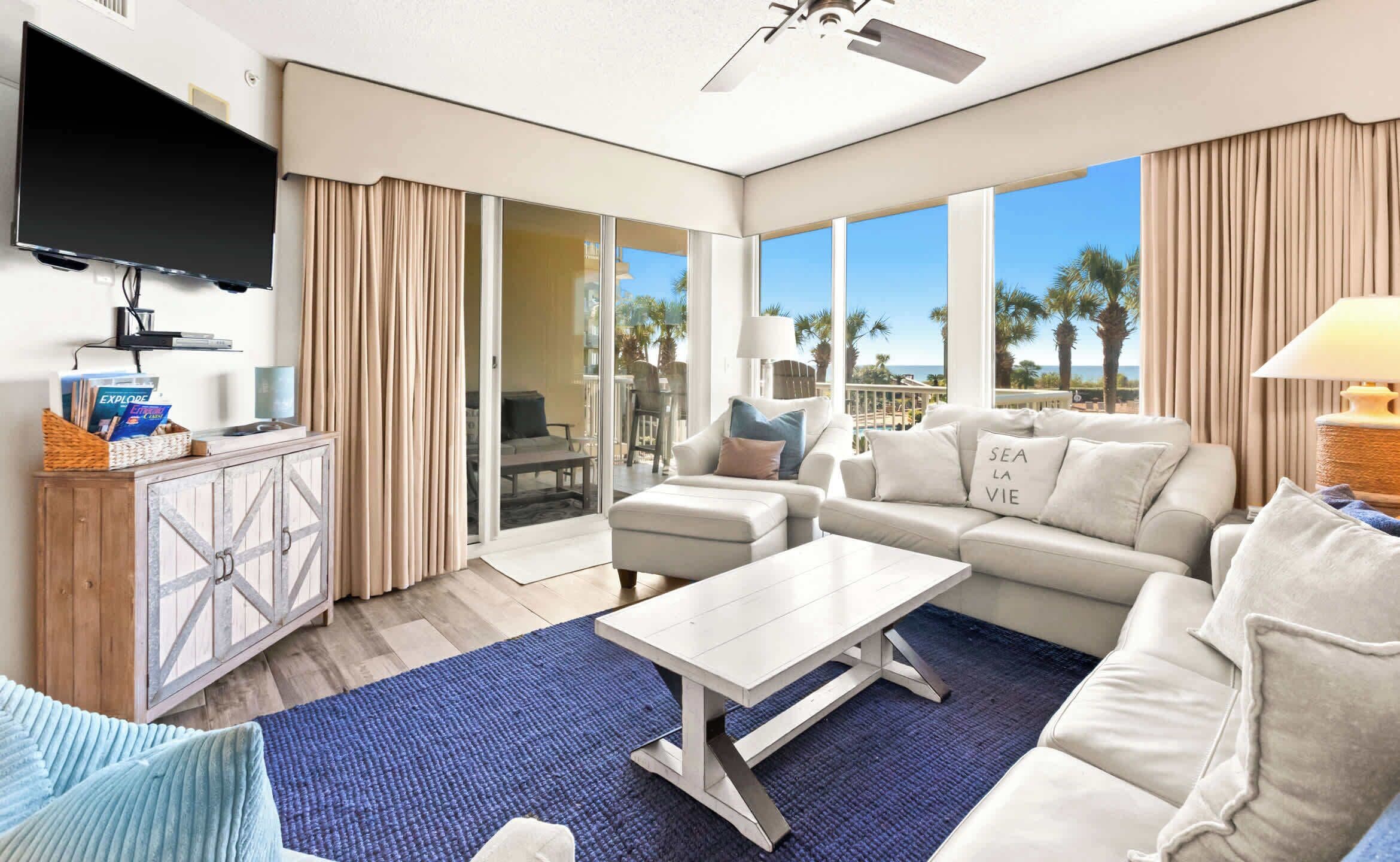 Una sala de estar moderna con un televisor de pantalla plana, un mueble de madera, un conjunto de sofás y vista a la playa.
