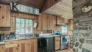 A kitchen with wooden cabinets, a stone wall, and a large window. - Riverfront Cabin w/Hot Tub : Near Mt. Rainier Sunrise entrance (Enumclaw)