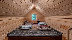 A cozy attic room with wooden walls, a sloped ceiling, and a small window. There are three patterned cushions on the floor and a small speaker on the wall. - Riverfront Cabin w/Hot Tub : Near Mt. Rainier Sunrise entrance (Enumclaw)