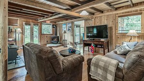 A cozy cabin interior with a fireplace, leather sofas, a TV, and wooden walls. - Riverfront Cabin w/Hot Tub : Near Mt. Rainier Sunrise entrance (Enumclaw)