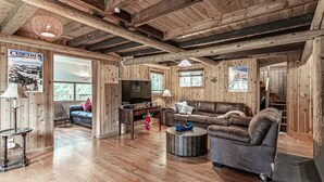 A rustic cabin interior with wooden walls and floors, a leather sofa, a television, and a fireplace. - Riverfront Cabin w/Hot Tub : Near Mt. Rainier Sunrise entrance (Enumclaw)