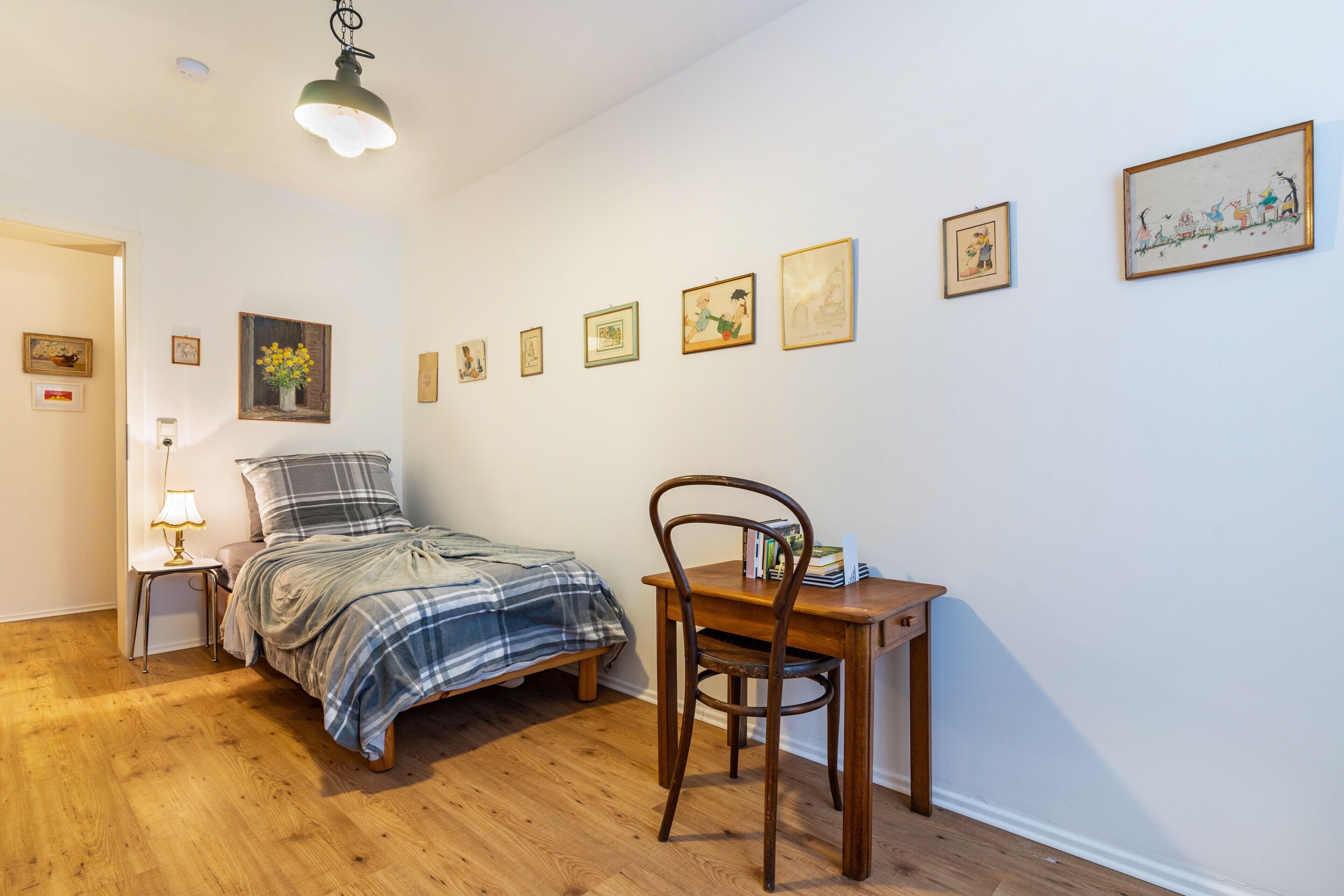 A bedroom with a bed, a desk, a chair, and several framed pictures on the wall.