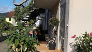 Um deck de madeira leva a um edifício com porta de garagem, cercado por plantas em vasos e uma escadaria.