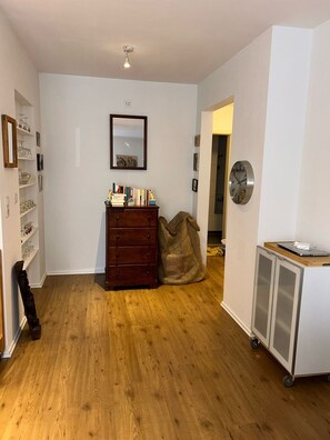 A room with wooden flooring, a wooden dresser, a mirror, a clock, and a cabinet with wheels.