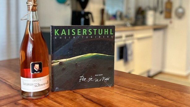 Uma garrafa de vinho Secco l'azzaro von Schwendi e um livro intitulado 'Kaiserstuhl' de Rainer Spaniel.