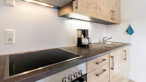 A modern kitchen with a built-in stove, a coffee maker, and wooden cabinets. - Apartment 'Ferienwohnung Torbrünnele' with Mountain View, Private Terrace and Wi-Fi (Bad Rippoldsau-Schapbach)