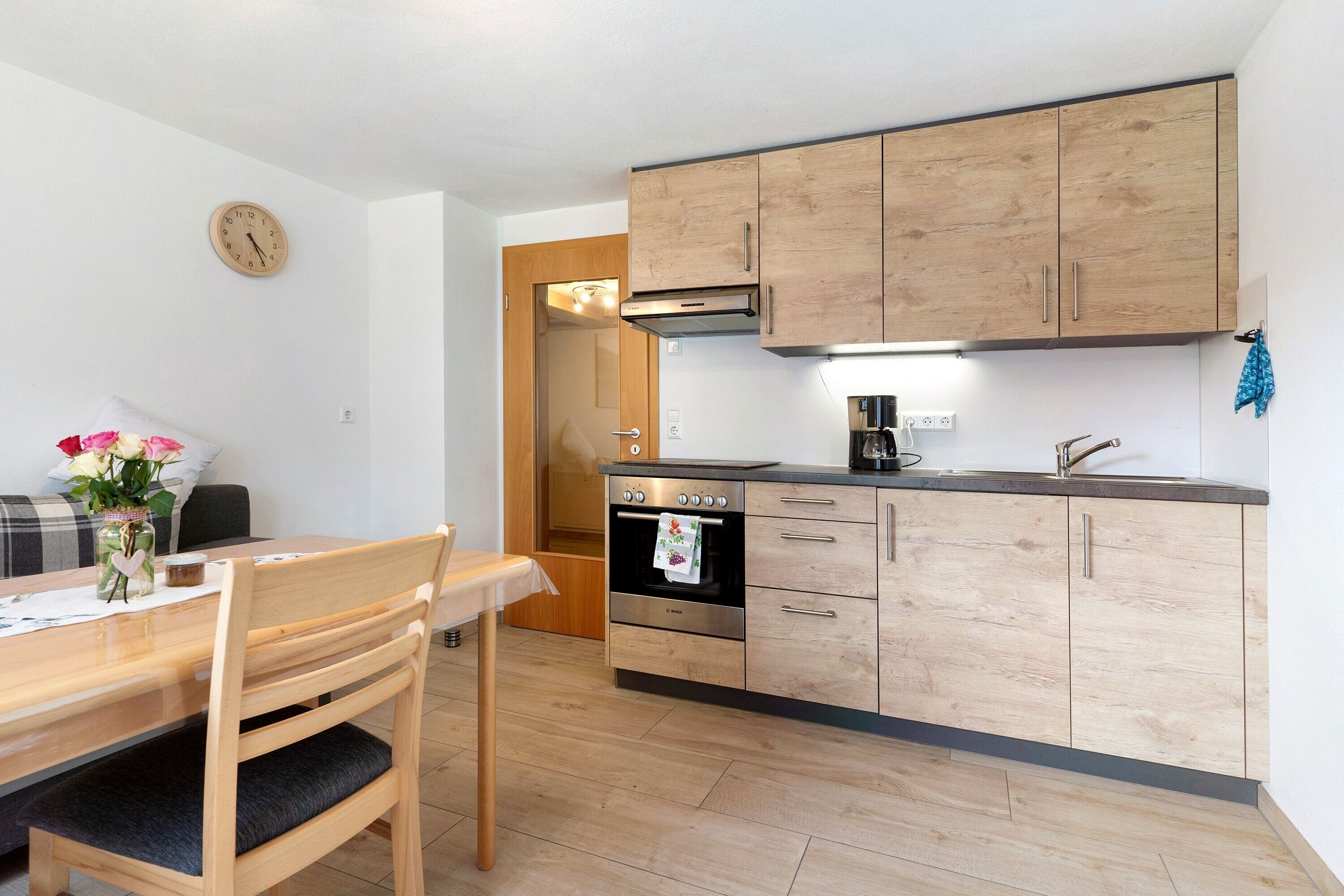 Une cuisine moderne avec des meubles en bois, un four encastré et un coin repas comprenant une table et des chaises.