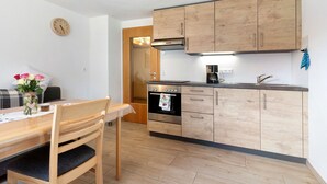 A modern kitchen with wooden cabinets, a built-in oven, and a dining area with a table and chairs. - Apartment 'Ferienwohnung Torbrünnele' with Mountain View, Private Terrace and Wi-Fi (Bad Rippoldsau-Schapbach)