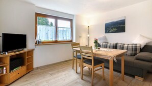A room with a television, wooden furniture, a table, a sofa, and a window with curtains. - Apartment 'Ferienwohnung Torbrünnele' with Mountain View, Private Terrace and Wi-Fi (Bad Rippoldsau-Schapbach)