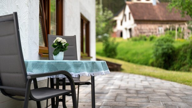 A patio with a table and chair, a potted plant, and a view of a traditional house in the background. - Apartment 'Ferienwohnung Torbrünnele' with Mountain View, Private Terrace and Wi-Fi (Bad Rippoldsau-Schapbach)