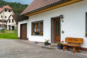 Un bâtiment blanc avec une porte et des fenêtres marron, un banc en bois et des plantes en pot.