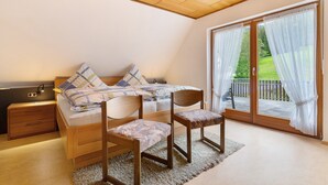 Quarto com cama, duas cadeiras de madeira, mesa de cabeceira e uma grande porta de vidro deslizante que dá para uma área externa.