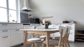 A kitchen with a round wooden table, four chairs, a stove, a sink, and a window. - Apartment 'Ferienwohnung Traumblick' with Balcony and Wi-Fi (Reesdorf)
