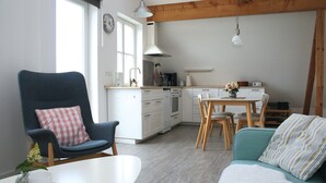 A modern kitchen with white cabinets, a dining area with a table and chairs, a blue armchair with a checkered pillow, and a teal sofa with a striped pillow. - Apartment 'Ferienwohnung Traumblick' with Balcony and Wi-Fi (Reesdorf)