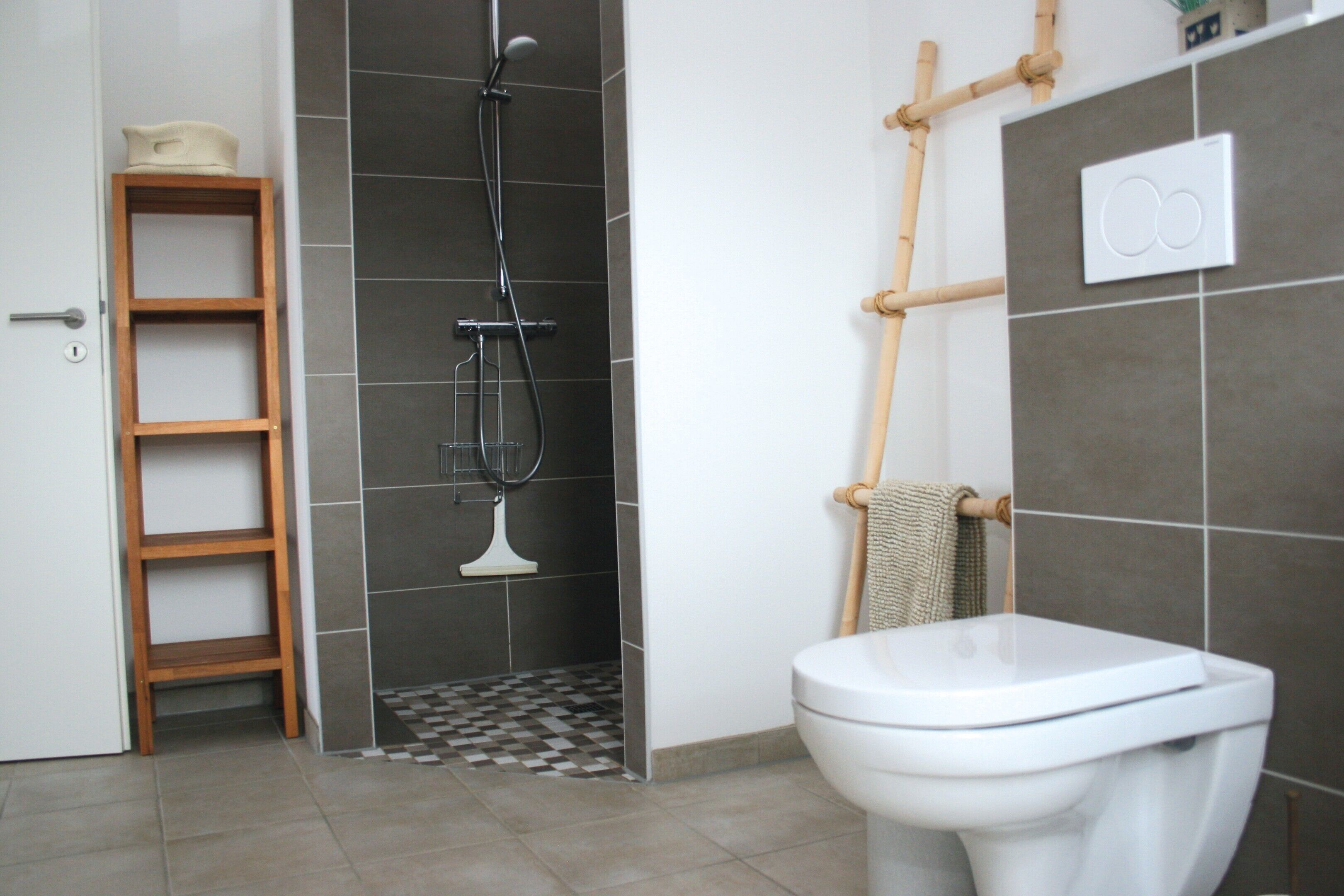 Un baño con inodoro, ducha, estante de madera y barra para toallas.