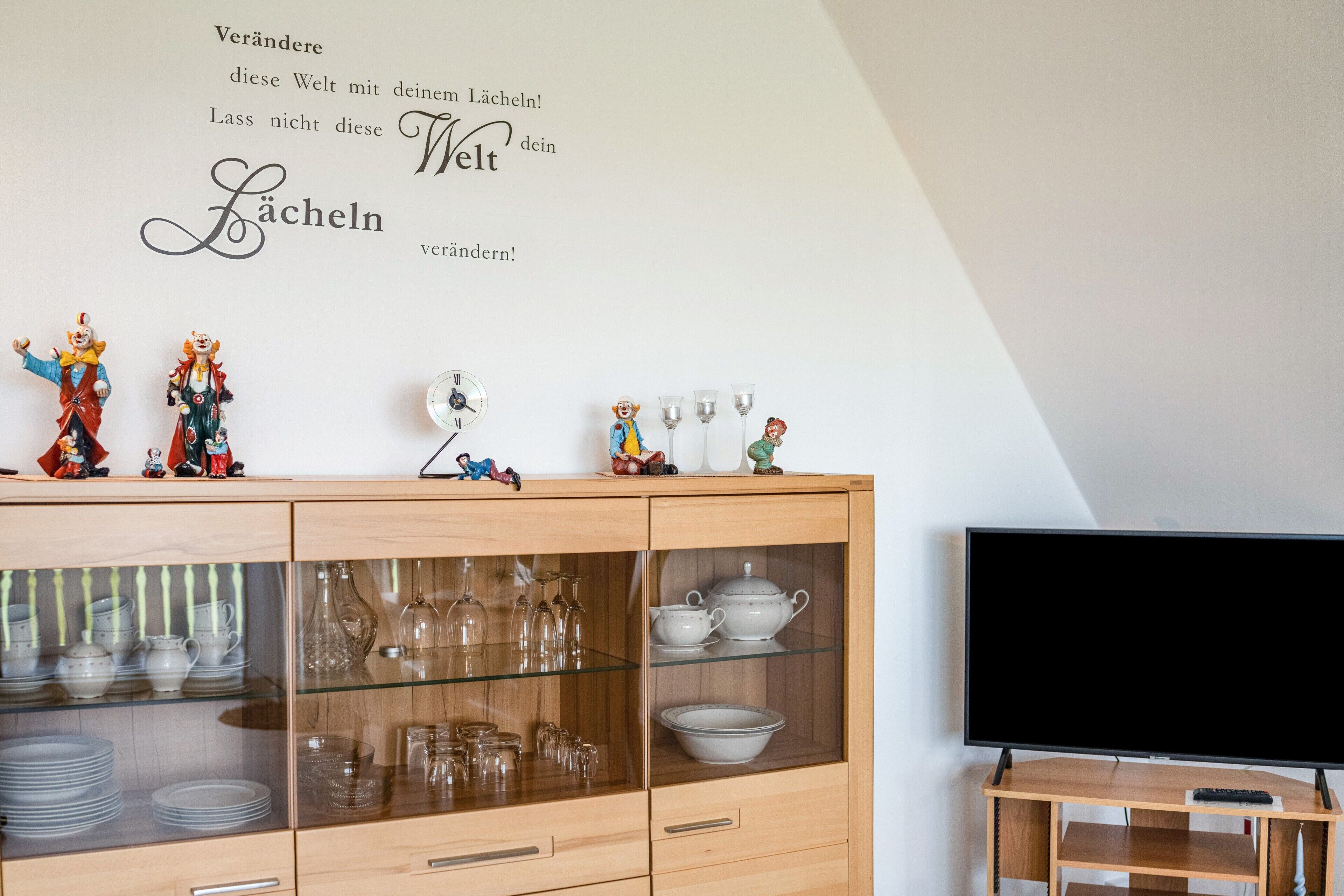 Ein Zimmer mit einem Holzschrank, der Gläser, einen Flachbildfernseher und dekorative Figuren beherbergt.