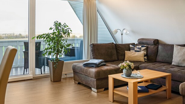 Een moderne woonkamer met een bank, een salontafel, een potplant en uitzicht door een groot raam.
