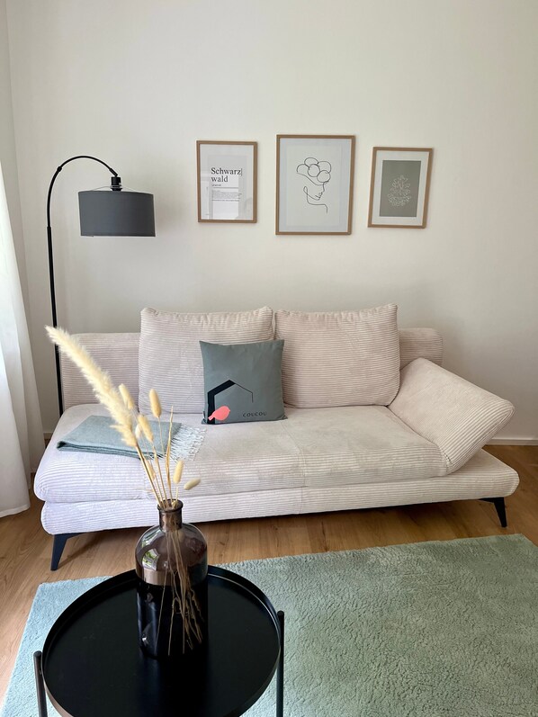 Un salon avec un canapé, une table basse ronde, un lampadaire et trois tableaux encadrés accrochés au mur.