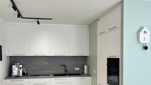 Una cocina moderna con armarios blancos, un grifo negro y un horno empotrado. Hay una mesa de comedor con sillas y un reloj de pared.