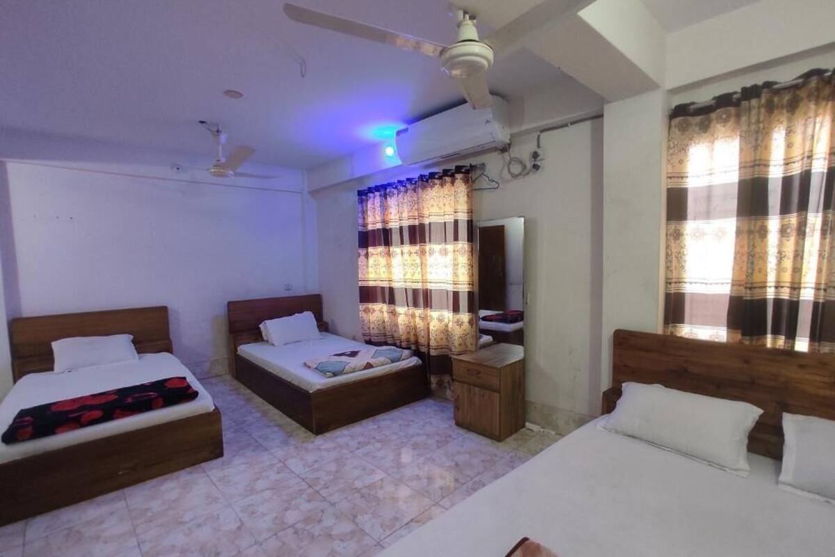 Une chambre d’hôtel avec deux lits, un ventilateur de plafond, un appareil de climatisation, un petit meuble en bois et des rideaux.