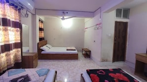Un dormitorio pequeño y bien iluminado con dos camas individuales, cabecera de madera, mesita de noche, armario y ventilador de techo.