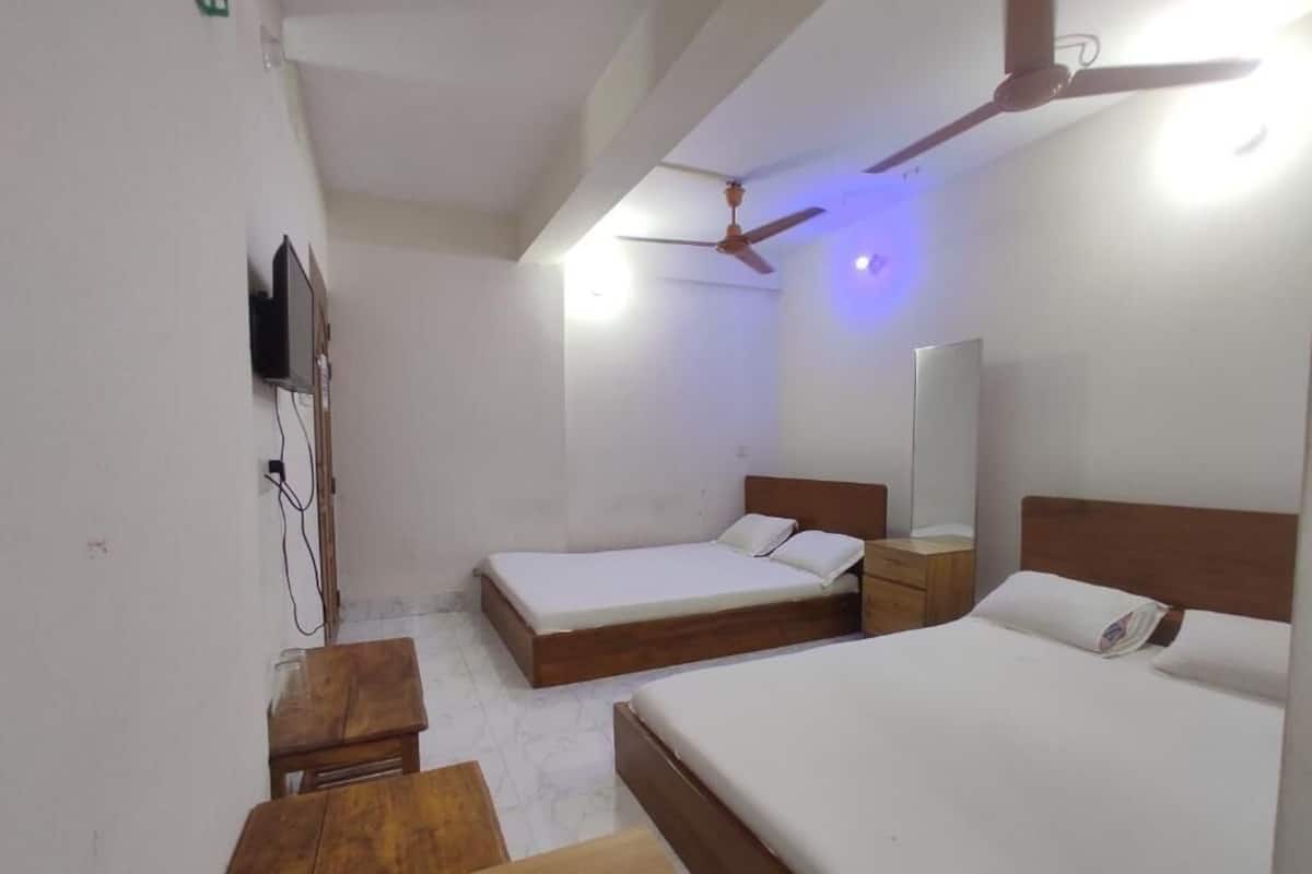 Une chambre d’hôtel avec deux lits simples, un bureau en bois, une télévision et un ventilateur de plafond.